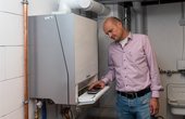 Hausbesitzer Bernhard Ruth zeigt bei geöffneter Frontklappe der Wärmepumpen-Inneneinheit die Systembedieneinheit für den Fachmann: die Logamatic HMC300. (Bild: Buderus)