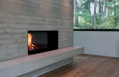 Eine offene Kaminwand aus Sichtbeton mit vorgelagerter Sitzbank sorgt für Gemütlichkeit an kalten Abenden. (Foto: nieberg architect)