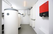 Gegenüber dem Pufferspeicher und Trinkwarmwasser-Standspeicher SBB 300 befinden sich der Wechselrichter (rot) und der Doppeltarifzähler. (Foto: Florian Arp für STIEBEL ELTRON)